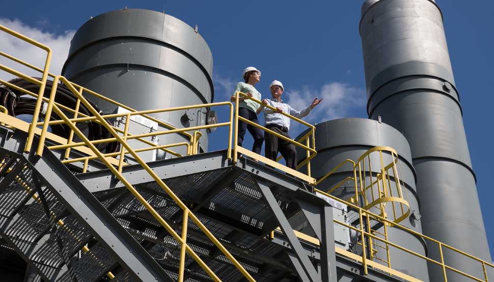 Two individuals at a manufacturing facility, wearing hard hats.