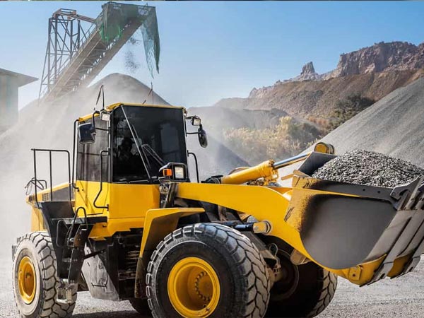 Large yellow construction vehicle carrying gravel at a quarry site