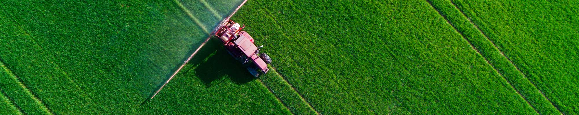 aerial view of a red tractor spraying crops in a green field
