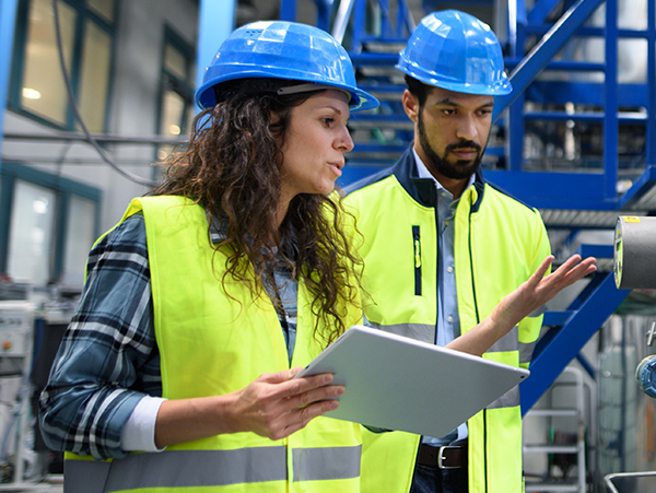 two workers in safety gear reviewing a tablet in a factory